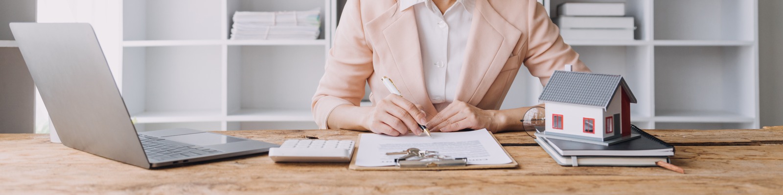An estate agency desk with a contract, calculator, laptop and keys